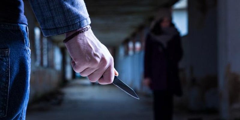 Imagem de um agressor com uma faca se preparando para abordar uma mulher